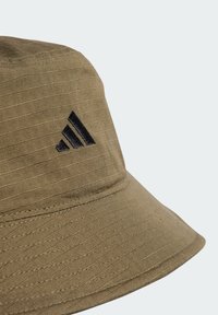 Khaki bucket hat made of textured fabric, featuring a slightly curved brim and a black Adidas logo on the front.