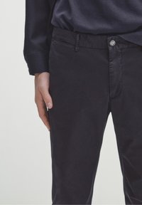 Pantaloni blu scuro realizzati in tessuto liscio, dotati di chiusura con bottone, passanti per cintura e tasche laterali, con una silhouette aderente.