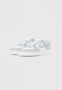 Białe i jasnoszare sneakersy niskie z sznurowadłami, perforowanymi noskami, logo Nike Swoosh po bokach i gumowymi podeszwami na jednolitym tle.