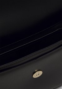 Wnętrze czarnej skórzanej torby o gładkiej fakturze. Posiada zapięcie na magnetyczny guzik oraz prosty, elegancki design. Nie widać dodatkowych przegródek.