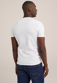 Weißes T-Shirt mit kurzen Ärmeln, taillierte Passform, glatte Textur, kombiniert mit blauen Jeans mit gelben Nähten und Gesäßtaschen.