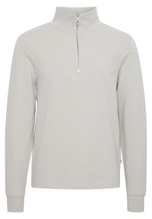Světle šedý svetr s dlouhým rukávem a vysokým límcem, s půlzipem, vyrobený z měkké tkaniny s hladkou texturou.
