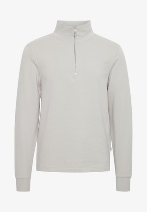 Světle šedý svetr s dlouhým rukávem a vysokým límcem, s půlzipem, vyrobený z měkké tkaniny s hladkou texturou.