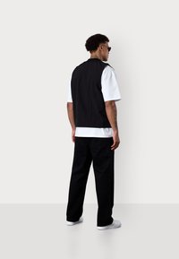 Schwarze ärmellose Weste über einem weißen T-Shirt, kombiniert mit lockeren schwarzen Hosen und weißen Sneakers. Sanfte Textur, minimalistisches Design.