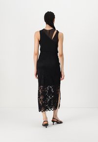 Must must have väljatäidetud ülemise osaga must kleit, millel on läbipaistev paneel, lillemustritega pitsiline seelik ja külgvoodrid, ning see on sobitatud mustade kontsadega sandaalidega.