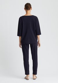 Marineblaues Zweiteiler-Outfit mit einem locker sitzenden Oberteil mit Dreiviertelärmeln und taillierten Hosen mit umgeschlagenen Säumen, gefertigt aus einem glatten Stoff.