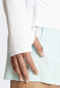 Biała koszula z długim rękawem z siateczkowym panelem i metką "AEROREADY", połączona z jasnosiwymi szortami o delikatnej teksturze i boczną kieszenią.