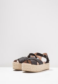 Czarne sandały na platformie z teksturowanymi paskami, z plecioną podeszwą w stylu espadryli oraz dekoracyjnym zapięciem.