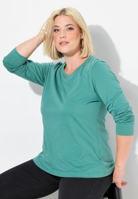Türkisfarbenes Langarm-T-Shirt mit Rundhalsausschnitt, aus weichem Baumwollmaterial und lockerer Passform. Verfügt über dezente Seitennähte.