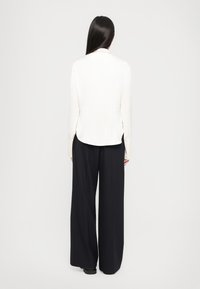 Pantaloni negri lungi și wide, asortați cu un top ușor de culoare ivorie, cu o margine curbată, mâneci lungi și un material moale, texturat.