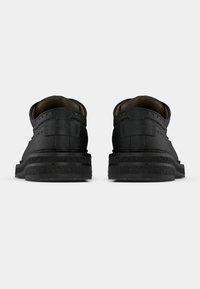 Chaussures en cuir noir avec finition texturée, présentant des détails perforés, une forme incurvée et une semelle en caoutchouc épaisse avec des accents superposés.