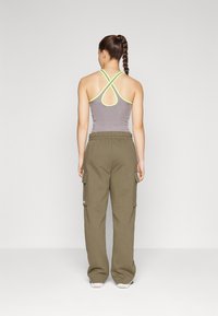 Top desportivo cinza com detalhes amarelos, design cruzado nas costas, combinado com calças cargo verde-oliva com bolsos laterais e cinturão elástico.