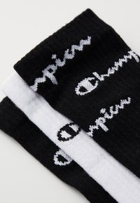 Calcetines de crew en blanco y negro con textura acanalada, con el logo de "Champion" en colores contrastantes en el lado de cada calcetín.
