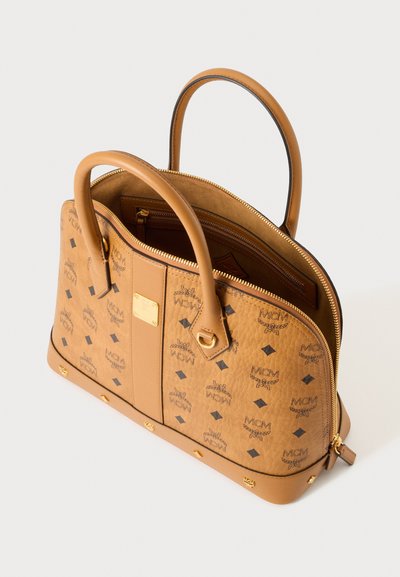 Sac à main MCM en cuir beige avec deux poignées, ferrures dorées, imprimé monogramme et fermeture éclair ouverte dévoilant un intérieur spacieux avec des poches.