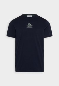 Tamsiai mėlynas medvilninis marškinėlis su apvaliu iškirpimu, puošiamas žaliai siuvinėtu krokodilo logotipu ir "LACOSTE" tekstu ant krūtinės.
