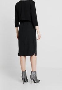 Svart klänning med trekvartslånga ärmar, med ett kort överdrag. Bärs med glittriga silvriga stövlar med ankeln, som visar en slank design.