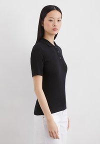 Zwarte geribbelde polo met korte mouwen, voorzien van een kraag en een drie-knopen sluiting. Soepele textuur, slim fit ontwerp en licht gebogen zoom.