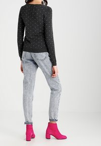 Szary sweter z długim rękawem w białe kropki, zestawiony z jasnoniebieskimi dżinsami i jaskrawo różowymi botkami za kostkę. Tkanina o teksturze, swobodny krój.