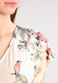 Blouse met korte mouwen van zachte stof, met een bloemmotief in verschillende kleuren, waaronder roze en groen, met een vogelontwerp op het borstgebied.