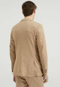 Beige texturerad blazer med ett subtilt rutmönster, enkel slits bak, och treknappar på ärmsluten. Skräddarsydd passform.