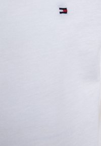 Hvit bomullsskjorte med et lite brodert logo i røde, hvite og blå nyanser. Stoffet er glatt med klassisk rund hals.