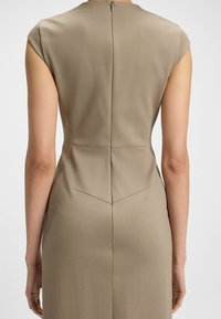 Sleeveless dress in light brown fabric, featuring a fitted bodice, vertical seams, and a back zipper, with a subtle textured finish.