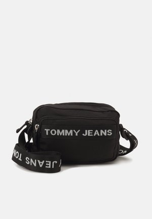 Černá obdélníková kabelka přes rameno s předním kapsou na zip a nastavitelným popruhem, oba s bílým nápisem "TOMMY JEANS".