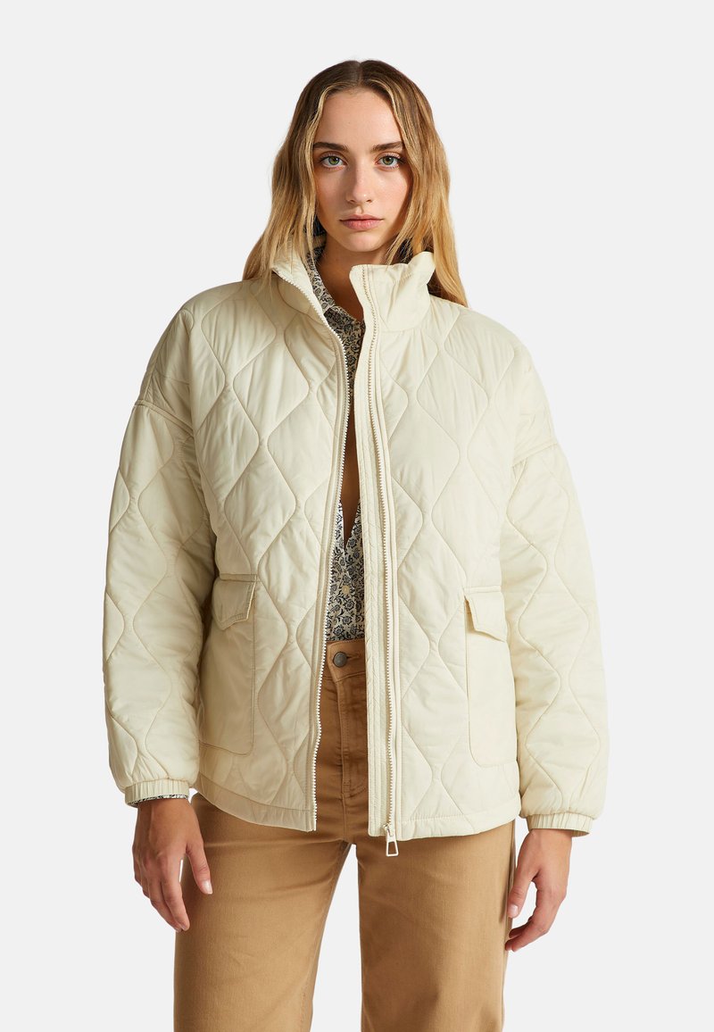 Prošívaná krémová bunda s vysokým límcem, dvěma předními kapsami a elastickými manžetami, se zipovým zapínáním a jemným diamantovým vzorem.