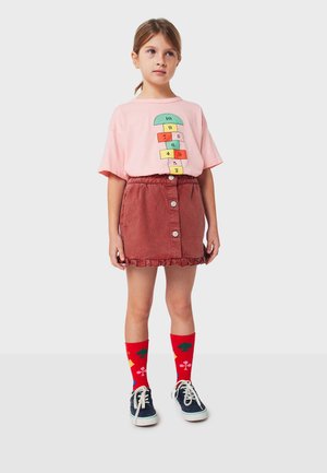 Pink cotton t-shirt with hopscotch graphic, rust-colored corduroy skirt with button front and frill, red socks with geometric patterns, and navy shoes.