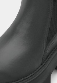 Čierne členkové čižmy s hladkým, lesklým koženým zvrškom, elastickými bočnými panelmi a hrubým, textúrovaným podpätkom. Diskrétny šev pozdĺž podrážky.