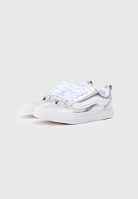 Adidași albi cu accente metalice argintii, design texturat, șireturi tradiționale și perle decorative pe partea din față. Stil low-top.