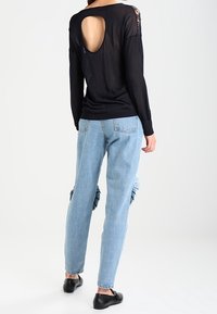 Schwarzer Strickpullover mit einem Rückenausschnitt und Spitzenakzenten, kombiniert mit hellblauen Jeans im Denim-Stil mit Rüschenakzenten an den Oberschenkeln.