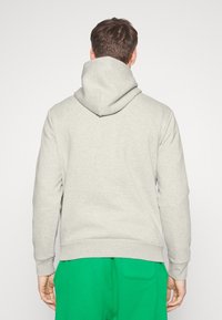 Jasnoszara bluza z kapturem o teksturowanym wykończeniu. Posiada luźny krój i ściągacze, zestawiona z zielonymi spodnimi.