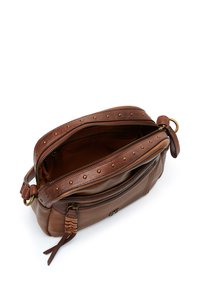 Sac en cuir marron à bandoulière avec des clous en laiton le long de la fermeture éclair, offrant un intérieur spacieux et un détail de tirette en cuir tressé.