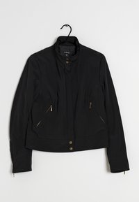 Schwarze Jacke mit Stehkragen, ausgestattet mit goldfarbenen Reißverschlusstaschen und Druckknöpfen an der Vorderseite. Glatter Stoff mit taillierter Silhouette.