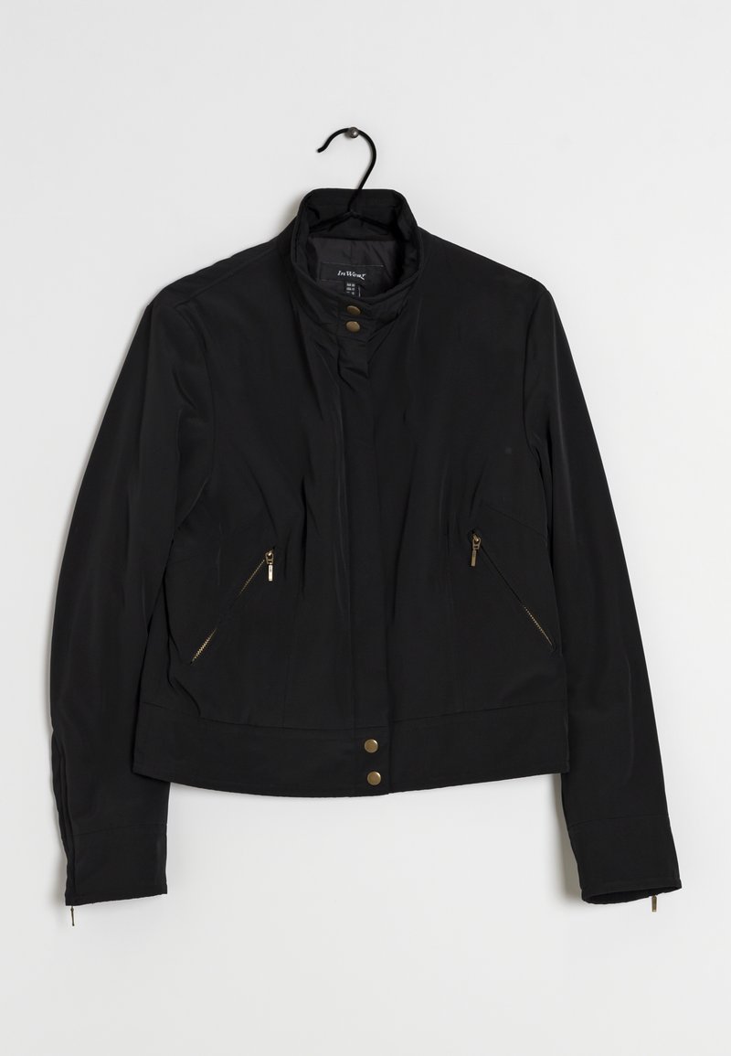 Schwarze Jacke mit Stehkragen, ausgestattet mit goldfarbenen Reißverschlusstaschen und Druckknöpfen an der Vorderseite. Glatter Stoff mit taillierter Silhouette.