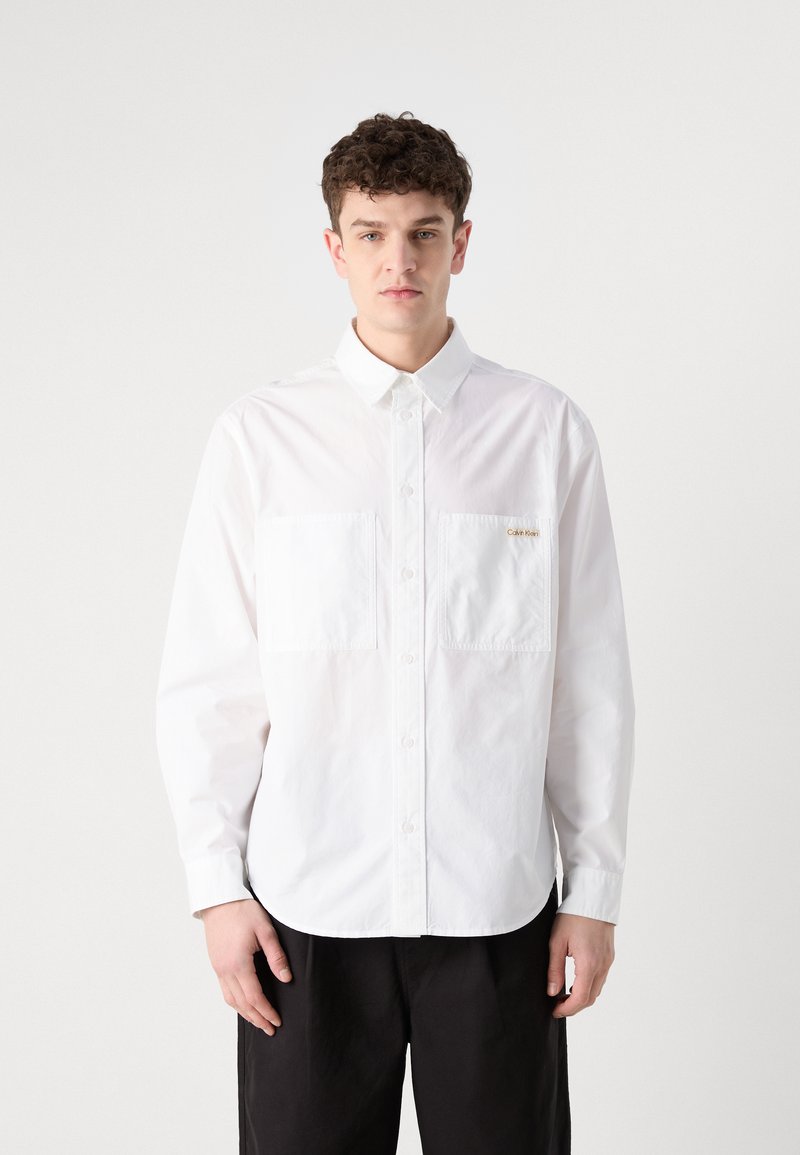 Camicia bianca con bottoni realizzata in cotone, dotata di due tasche sul petto, colletto classico e orlo curvo. Logo discreto sulla tasca.