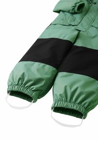 Zielony i czarny ocieplany kombinezon narciarski z elastycznymi mankietami i wbudowanymi paskami na stopy. Gładki, błyszczący materiał z designem w blokach kolorowych.