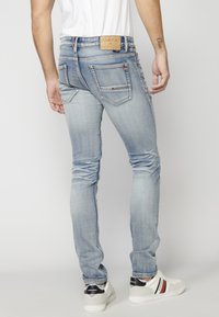 Světle modré skinny džíny s vybledlým vzhledem, designem s pěti kapsami, kontrastním prošíváním a hnědou koženou etiketou na pásku.
