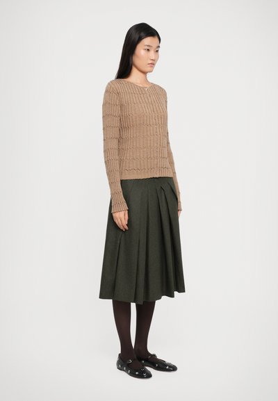 Beige knitted cardigan with textured pattern, button front; dark green pleated skirt, black shoes with decorative hardware, dark tights.