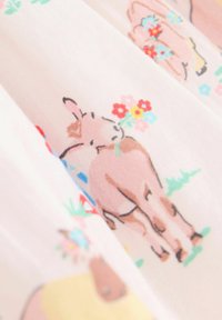 Tessuto di cotone con uno sfondo rosa pastello che presenta cavalli marroni, fiori e vegetazione illustrati in un motivo ripetitivo.
