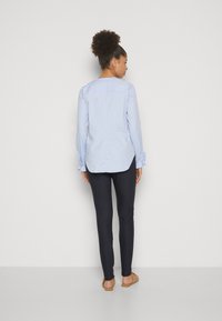 Camicia azzurra a maniche lunghe con taglio dritto, polsini abbottonati, texture sottile, e pantaloni navy scuri a vestibilità slim. In utilisant sandali piatti.