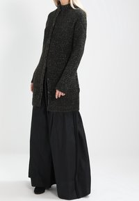 Long, dark textured cardigan with a high collar and front button closure, paired with wide black trousers. Soft knit fabric, simple design.
