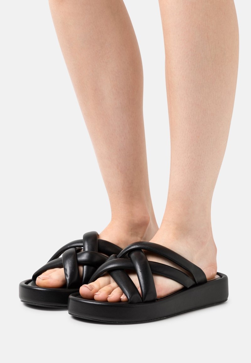 Sandales à enfiler noires avec une plateforme épaisse, un design de sangle entrelacée et une texture lisse, présentant un style à bout ouvert.