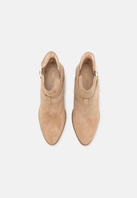 Bottines en suédine beige à bouts pointus, avec des sangles à boucle sur le côté et des semelles plates, présentées en vue de dessus sur un fond blanc.