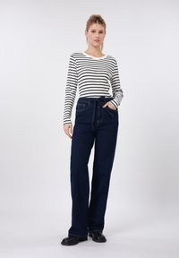 Μπλούζα με μακριά μανίκια ριγέ σε μαύρο και άσπρο, συνδυασμένη με σκούρα μπλε τζιν παντελόνι ψηλόμεσο, με φαρδιά μπατζάκια και ζώνη στη μέση. Απαλό ύφασμα, άνετη γραμμή.