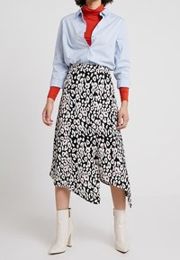 Asymetrická černá sukně s růžovým a bílým leopardím potiskem, v kombinaci se světle modrou košilí na knoflíky a červeným rolákem; modelka nosí bílé kotníkové boty.