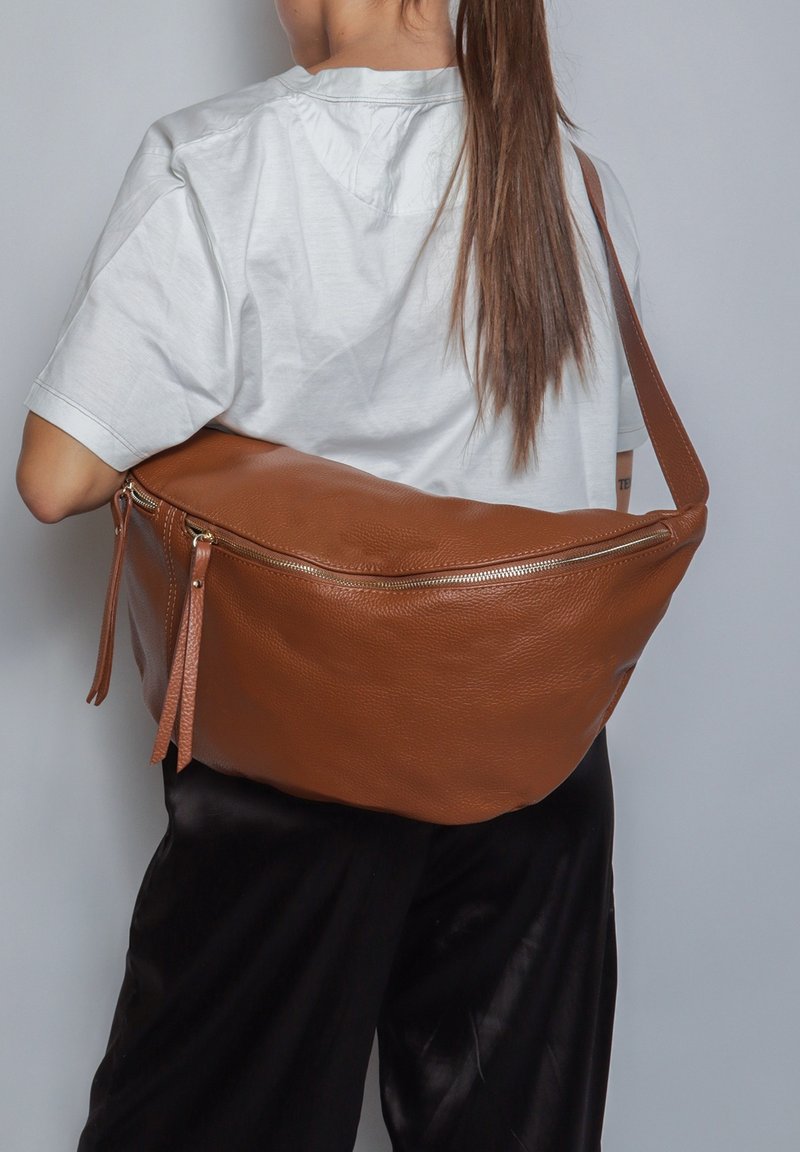 Borsa a spalla in pelle marrone con una superficie liscia, forma ampia e chiusura con zip decorata da frange. Indossata a tracolla.