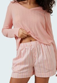 Rosa långärmad topp med V-ringning och strukturerat mönster, kombinerad med randiga rosa och vita shorts med knäppning fram och elastisk midja.