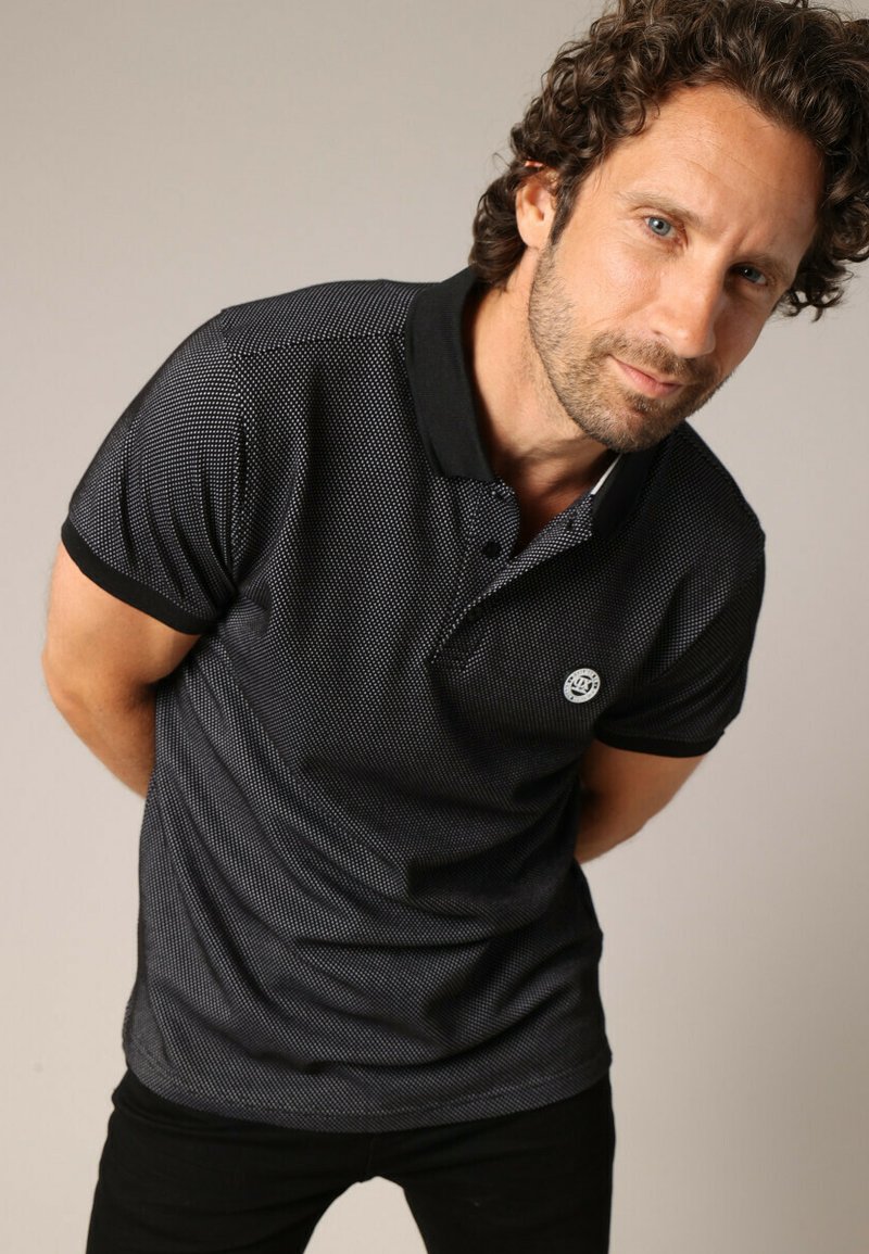 T-shirt polo noir avec un motif texturé, col noir et un petit logo sur la poitrine. Manches courtes et coupe ajustée.